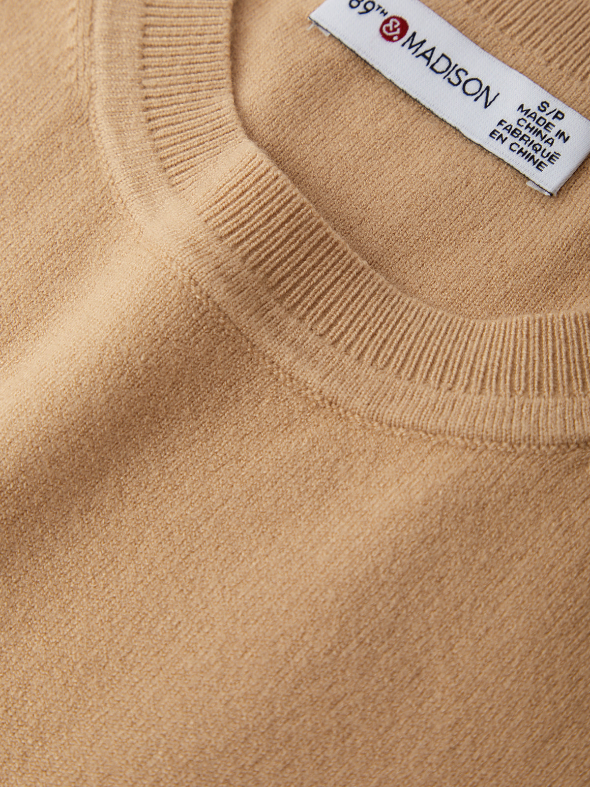 Close-up of a beige sweater with a brand label on the collar.