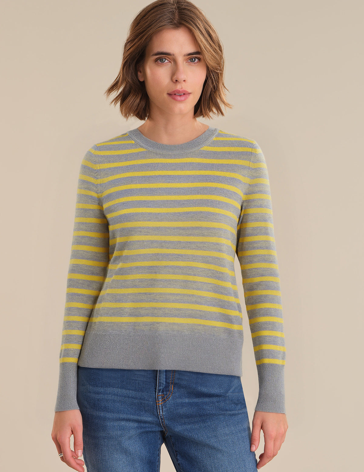 Woman wearing a gray and yellow striped sweater with blue jeans on a beige background