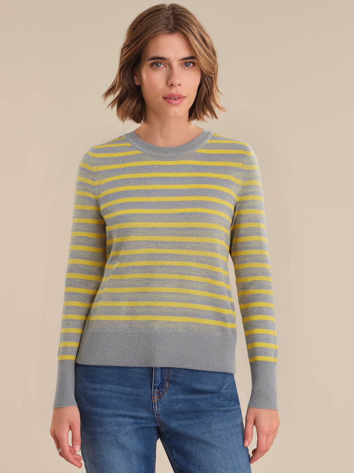Woman wearing a gray and yellow striped sweater with blue jeans on a beige background