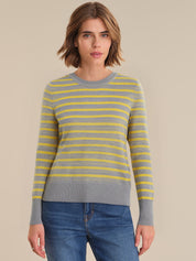 Woman wearing a gray and yellow striped sweater with blue jeans on a beige background