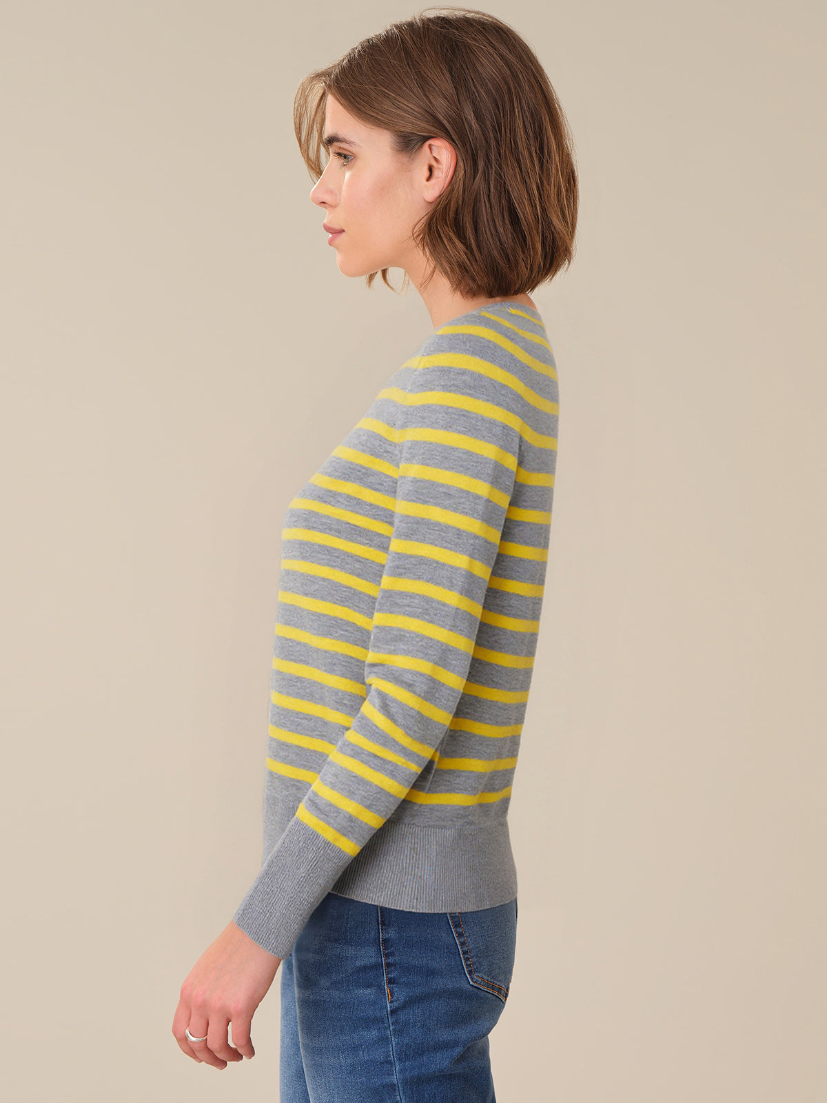 Woman wearing a gray and yellow striped sweater against a beige background