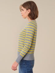 Woman wearing a gray and yellow striped sweater against a beige background