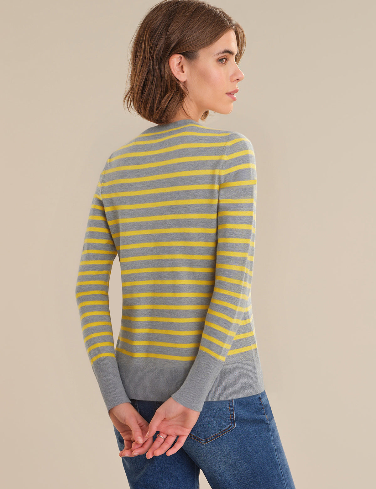 Woman wearing a gray and yellow striped sweater against a beige background