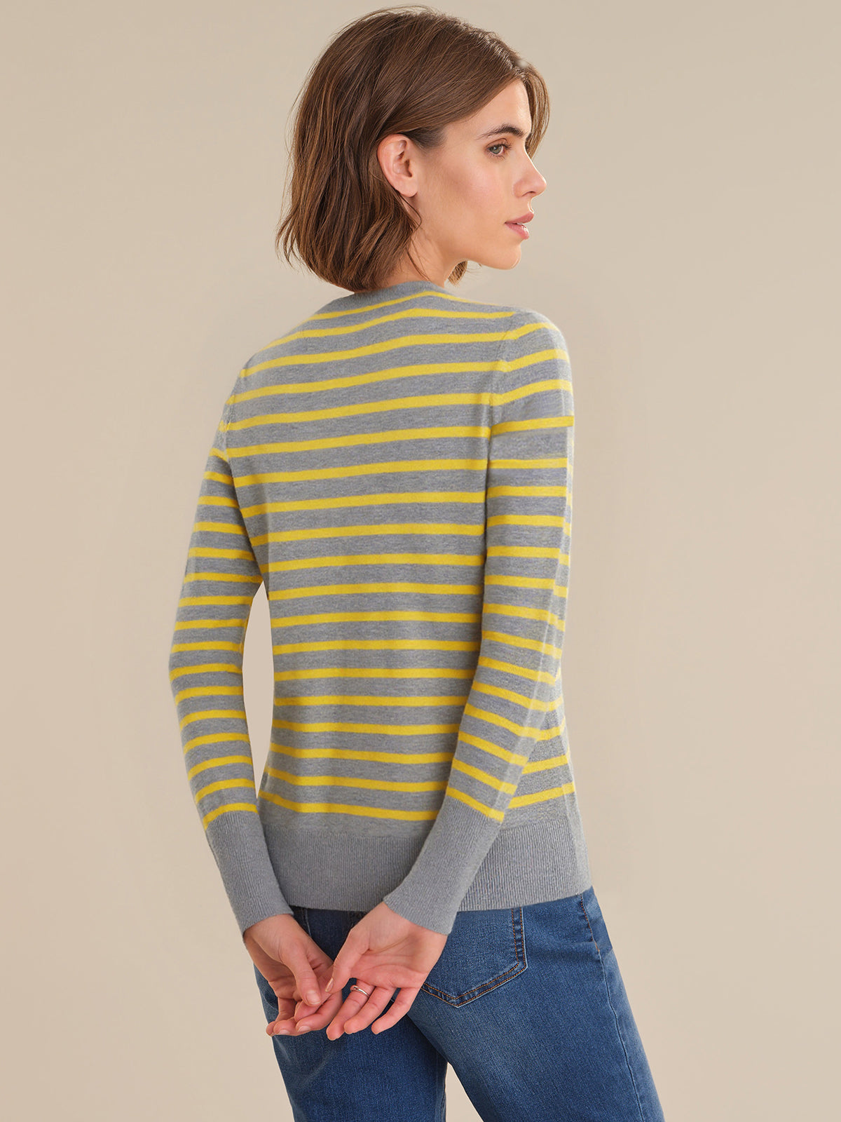 Woman wearing a gray and yellow striped sweater against a beige background