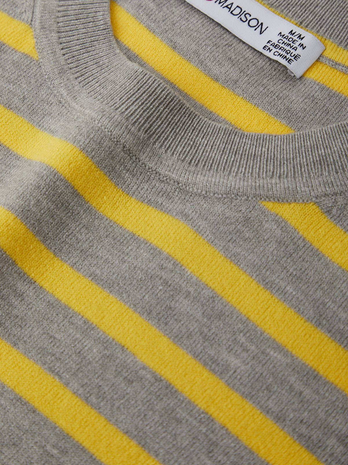 Close-up of a gray sweater with yellow stripes and a visible label.