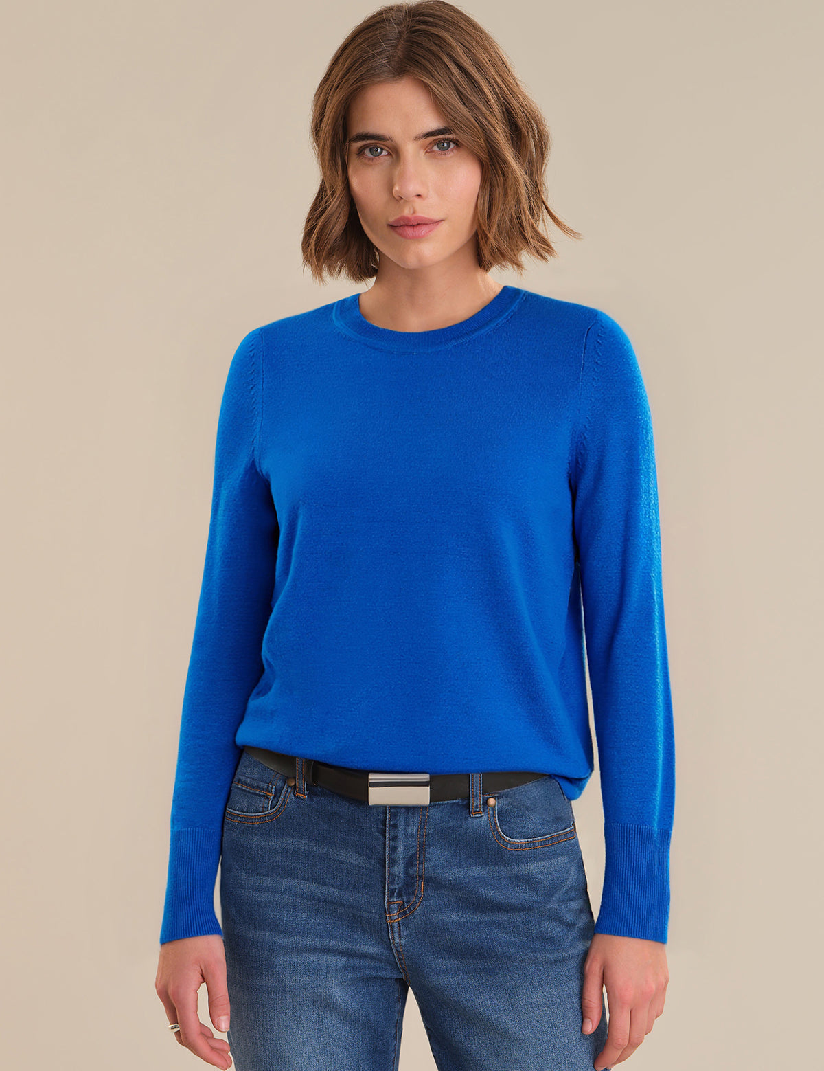Woman wearing a blue sweater and jeans on a beige background