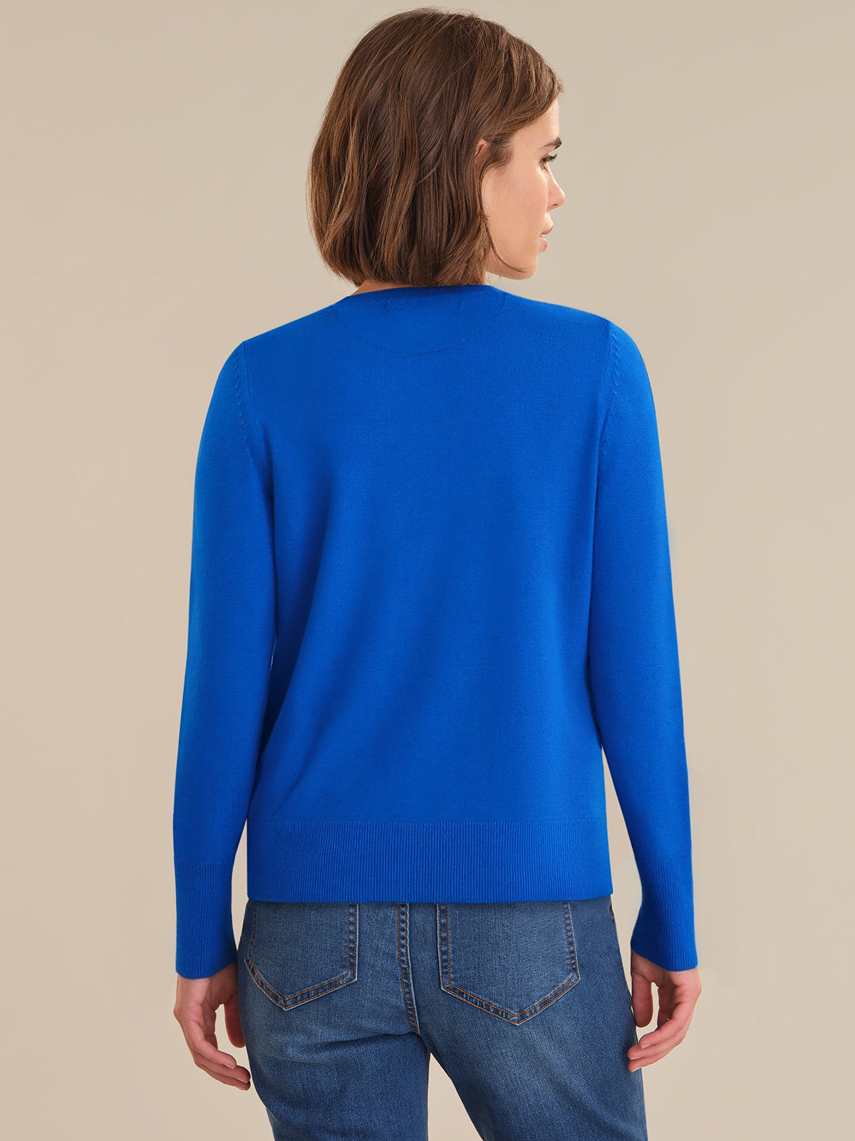 Person wearing a blue sweater and jeans against a beige background