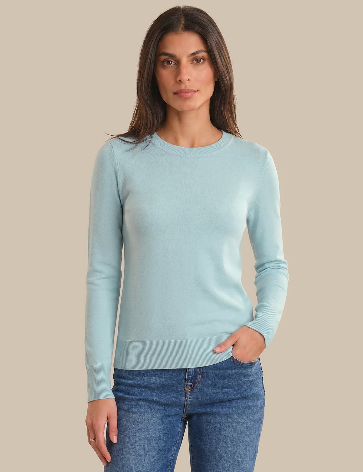 Woman wearing a light blue sweater and jeans on a beige background