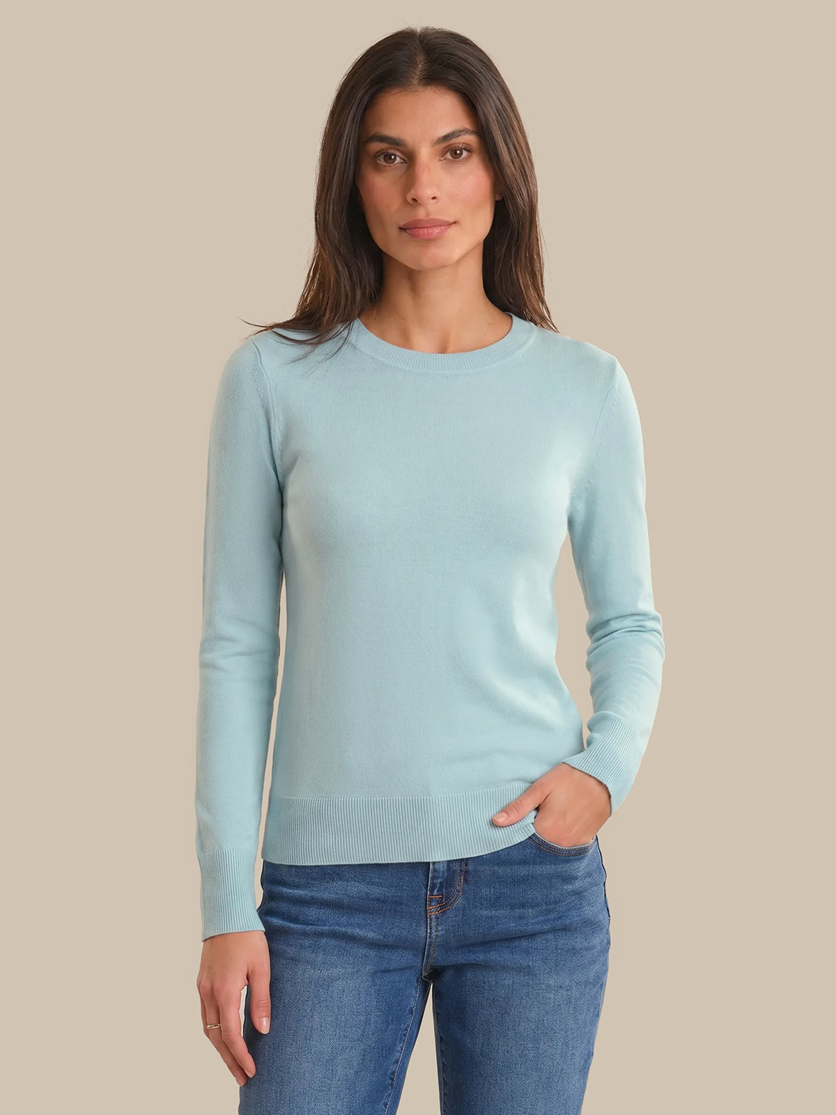 Woman wearing a light blue sweater and jeans on a beige background