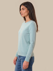 Woman wearing a light blue sweater and blue jeans against a beige background