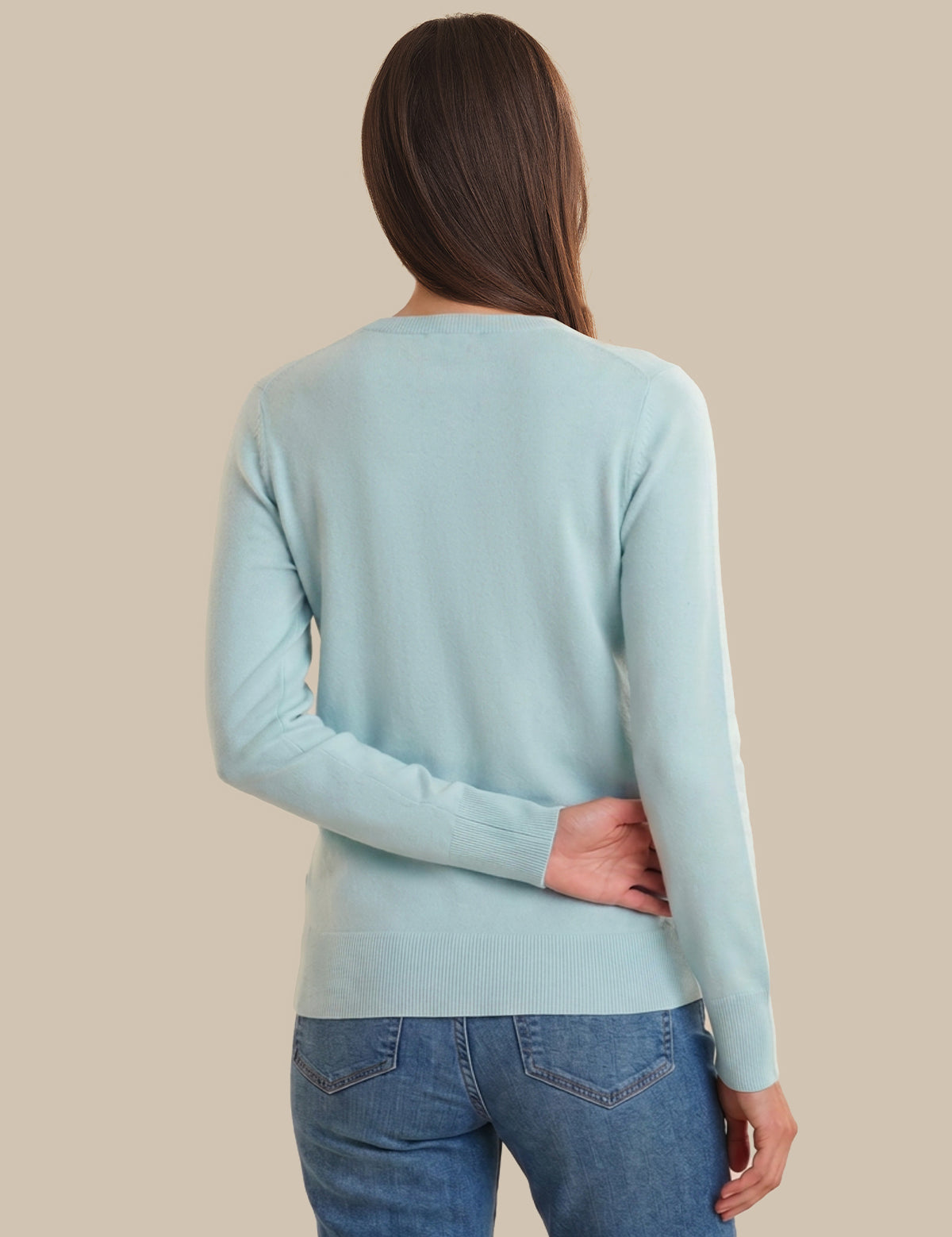 Woman wearing a light blue sweater and blue jeans against a beige background