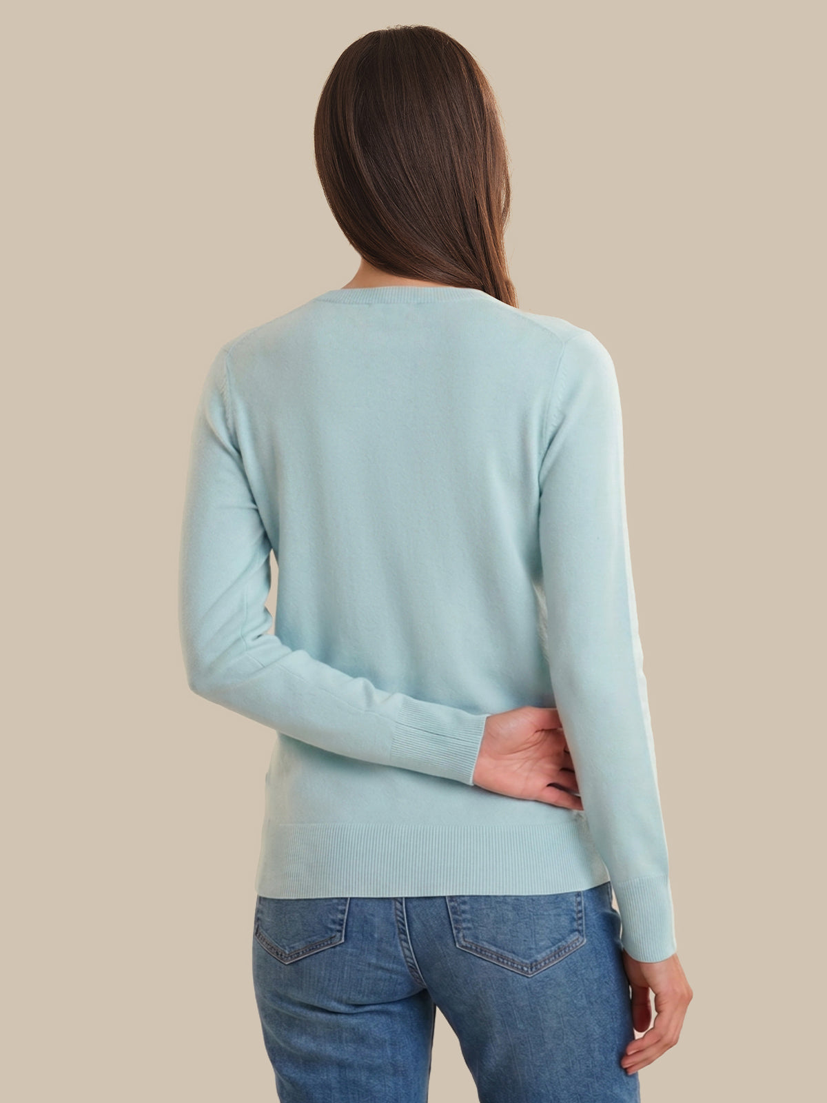 Woman wearing a light blue sweater and blue jeans against a beige background