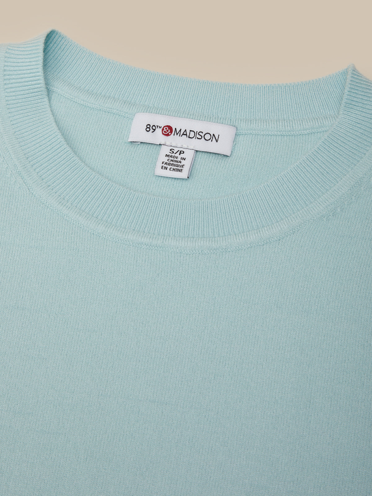 Light blue sweater with a brand label on a beige background