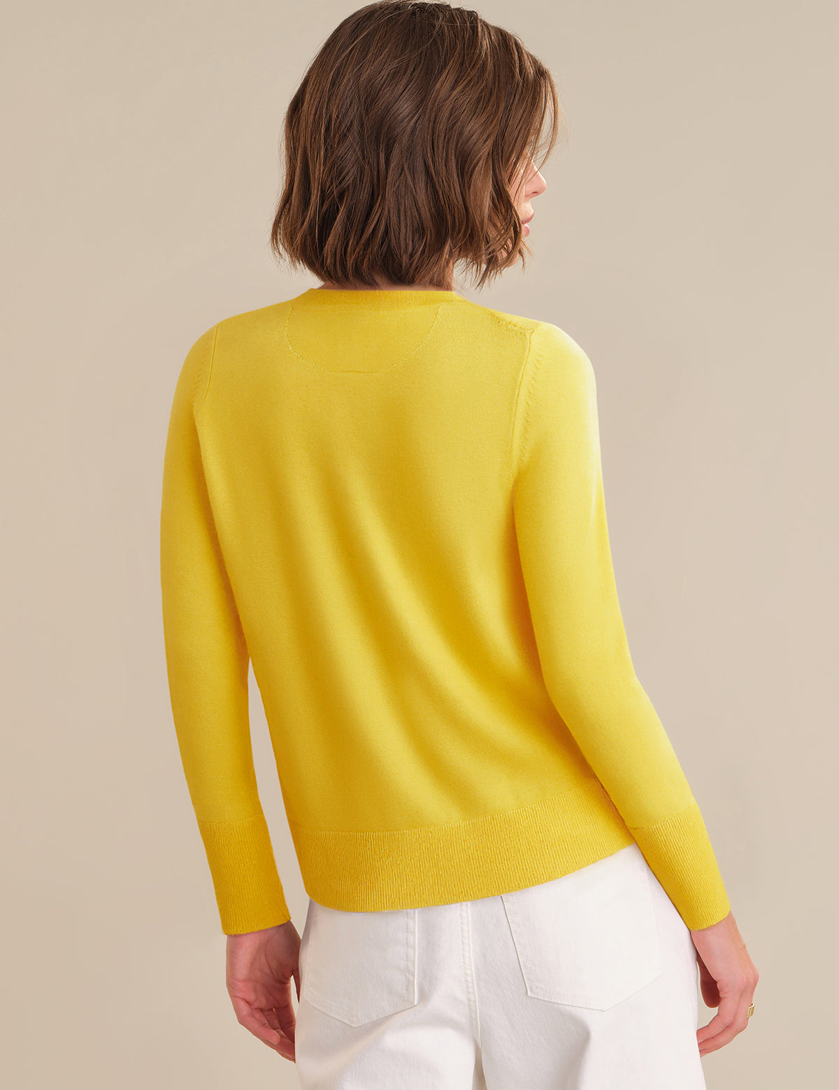 Person wearing a yellow sweater and white pants on a beige background