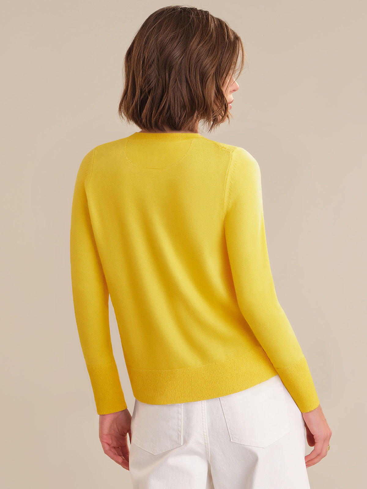 Person wearing a yellow sweater and white pants on a beige background