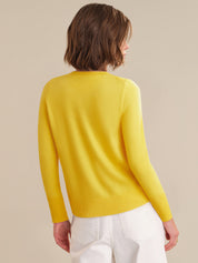 Person wearing a yellow sweater and white pants on a beige background