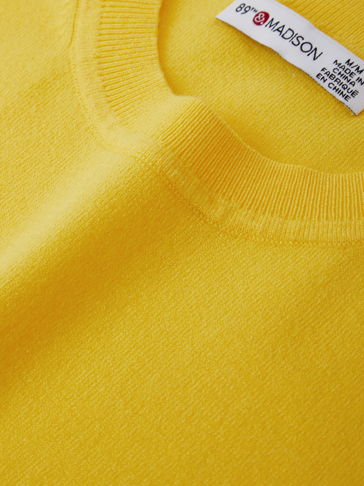 Close-up of a yellow sweater with a brand label on the collar.