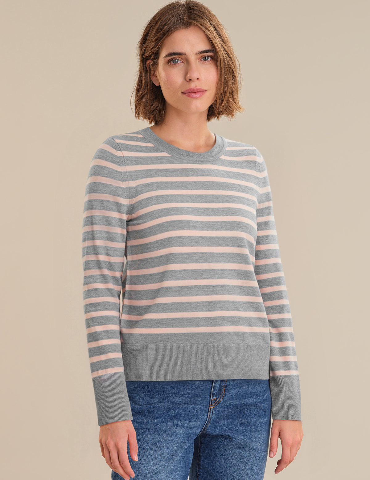 Woman wearing a striped sweater and jeans on a beige background