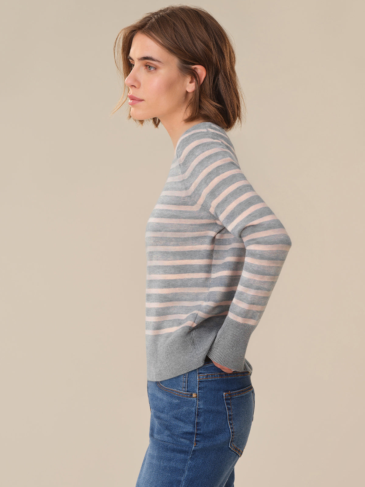 Woman wearing a striped sweater and jeans against a beige background