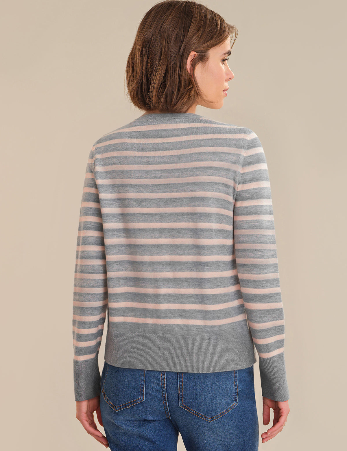 Person wearing a striped sweater and blue jeans against a beige background