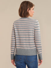 Person wearing a striped sweater and blue jeans against a beige background