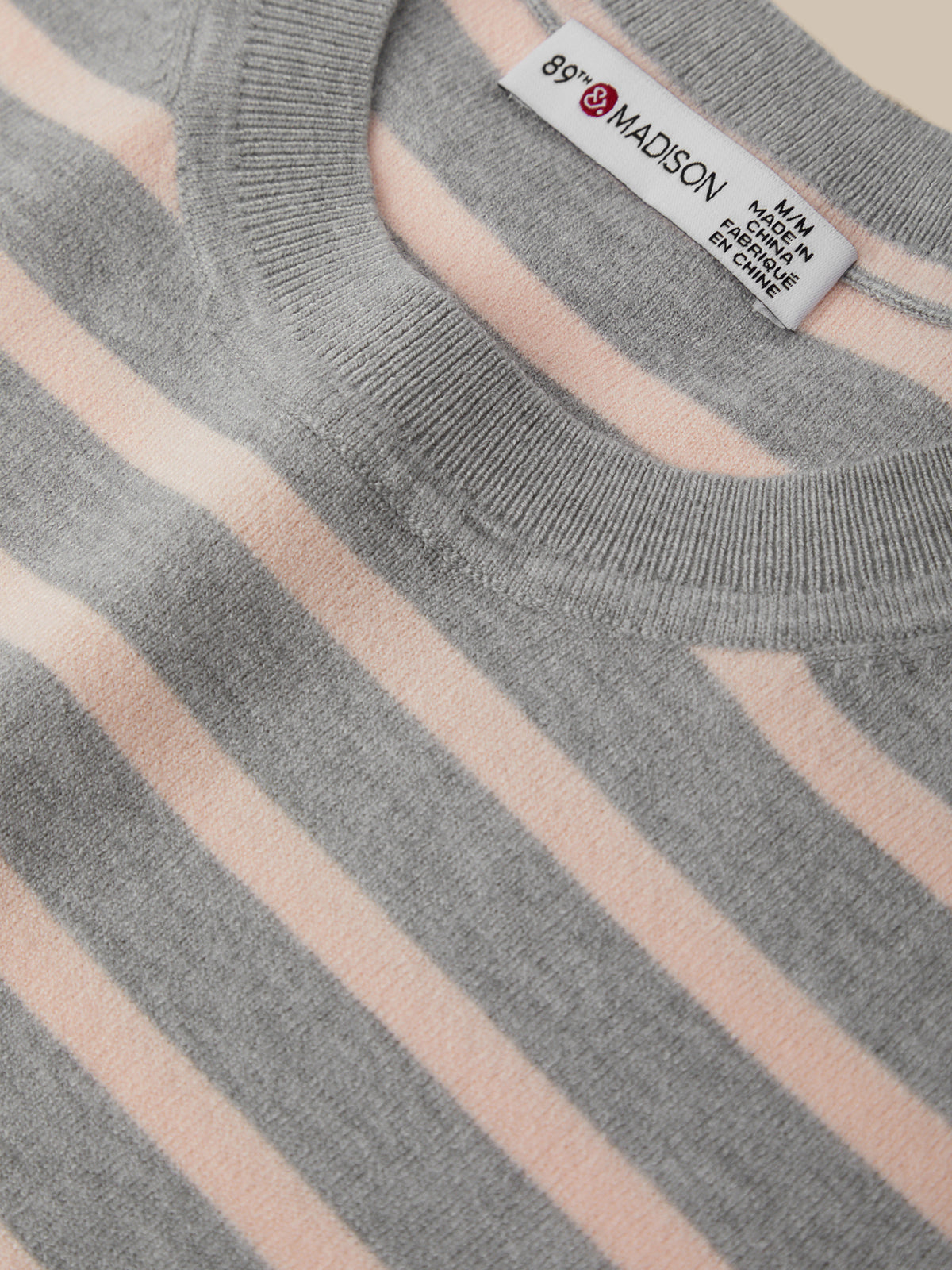 Close-up of a gray and pink striped sweater with a label on a white background