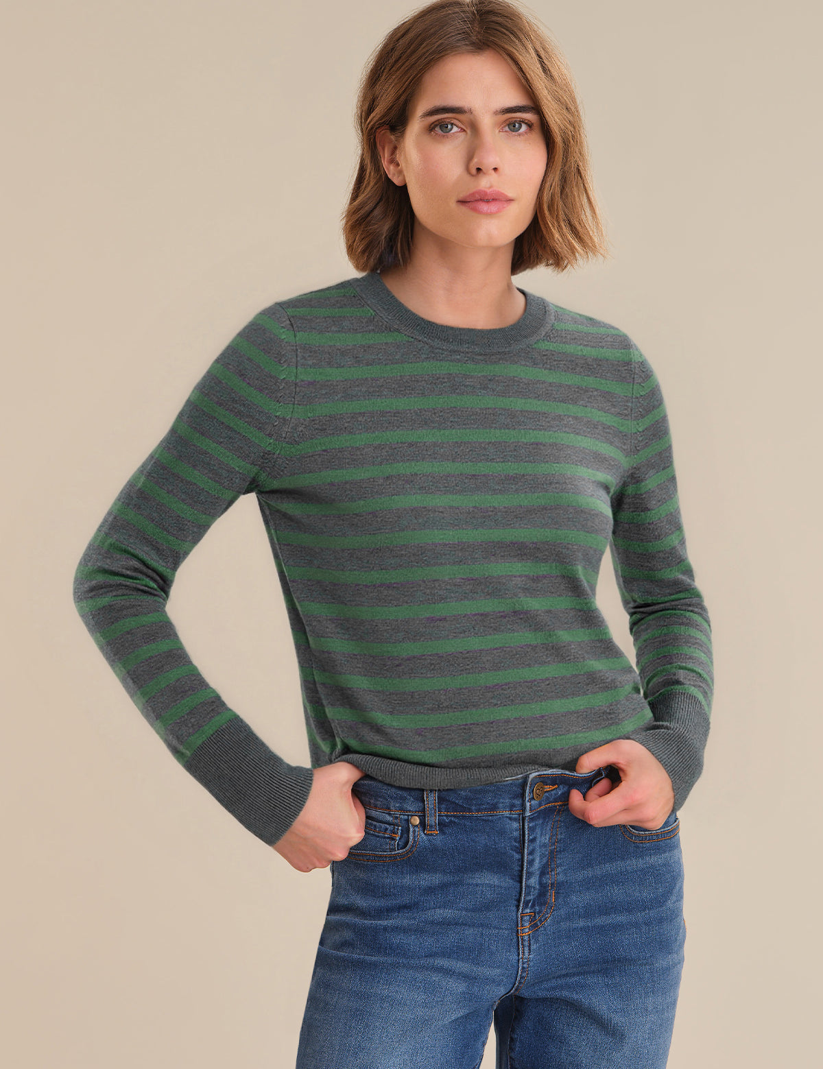 Woman wearing a green and gray striped sweater with blue jeans on a beige background