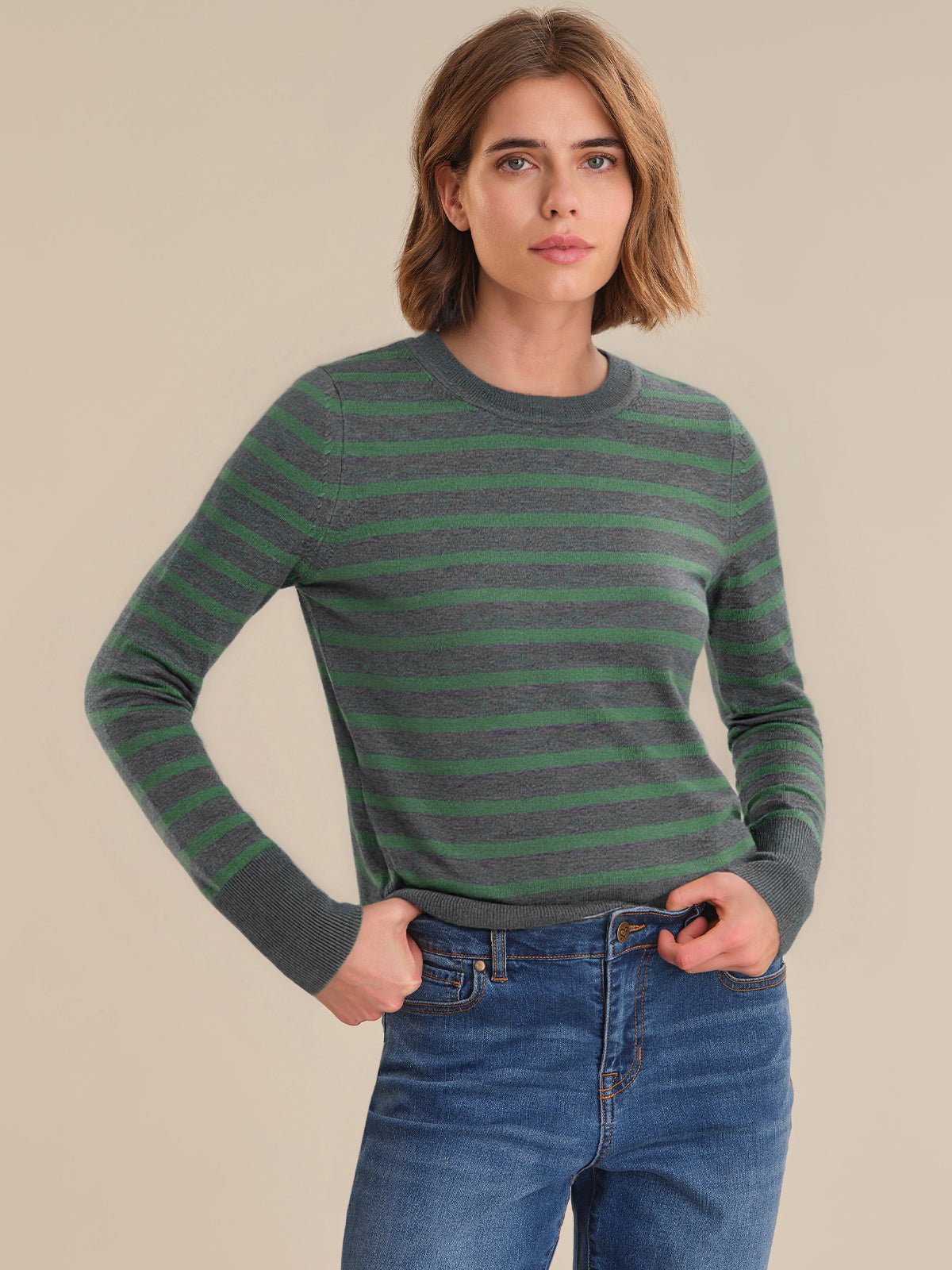 Woman wearing a green and gray striped sweater with blue jeans on a beige background