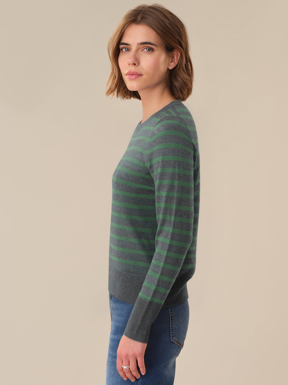 Woman wearing a green and gray striped sweater against a beige background