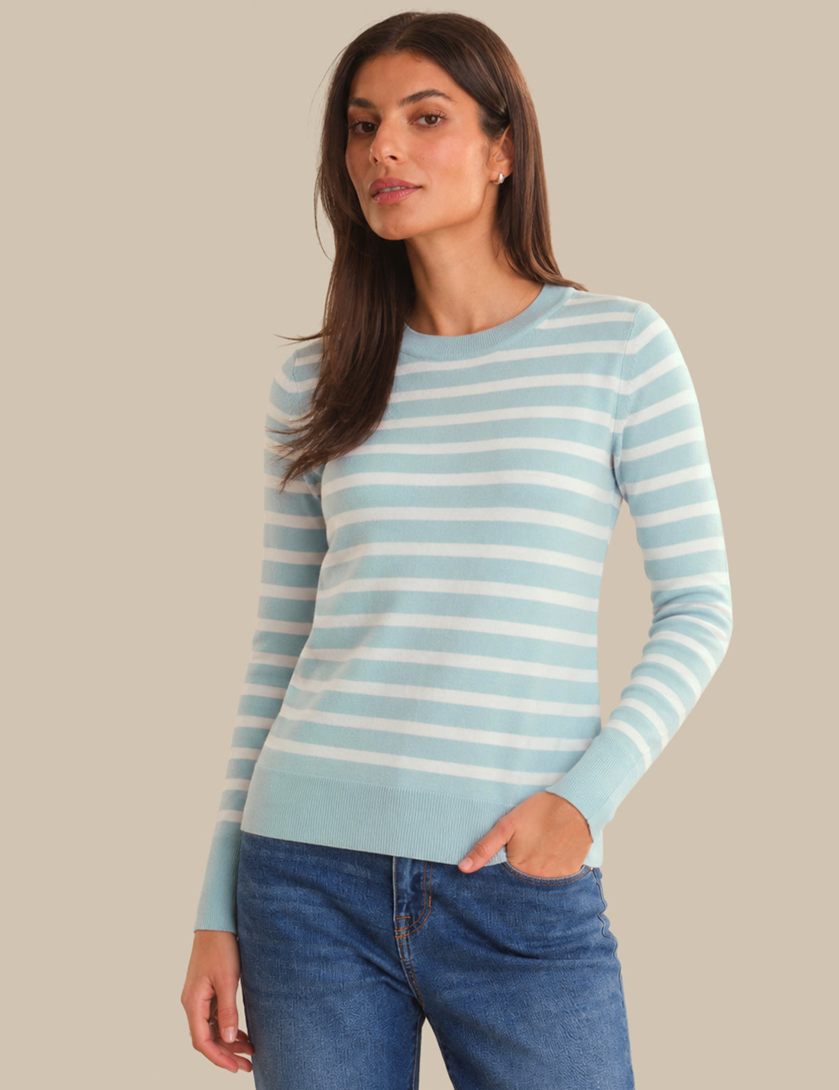 Woman wearing a light blue and white striped sweater with blue jeans on a beige background