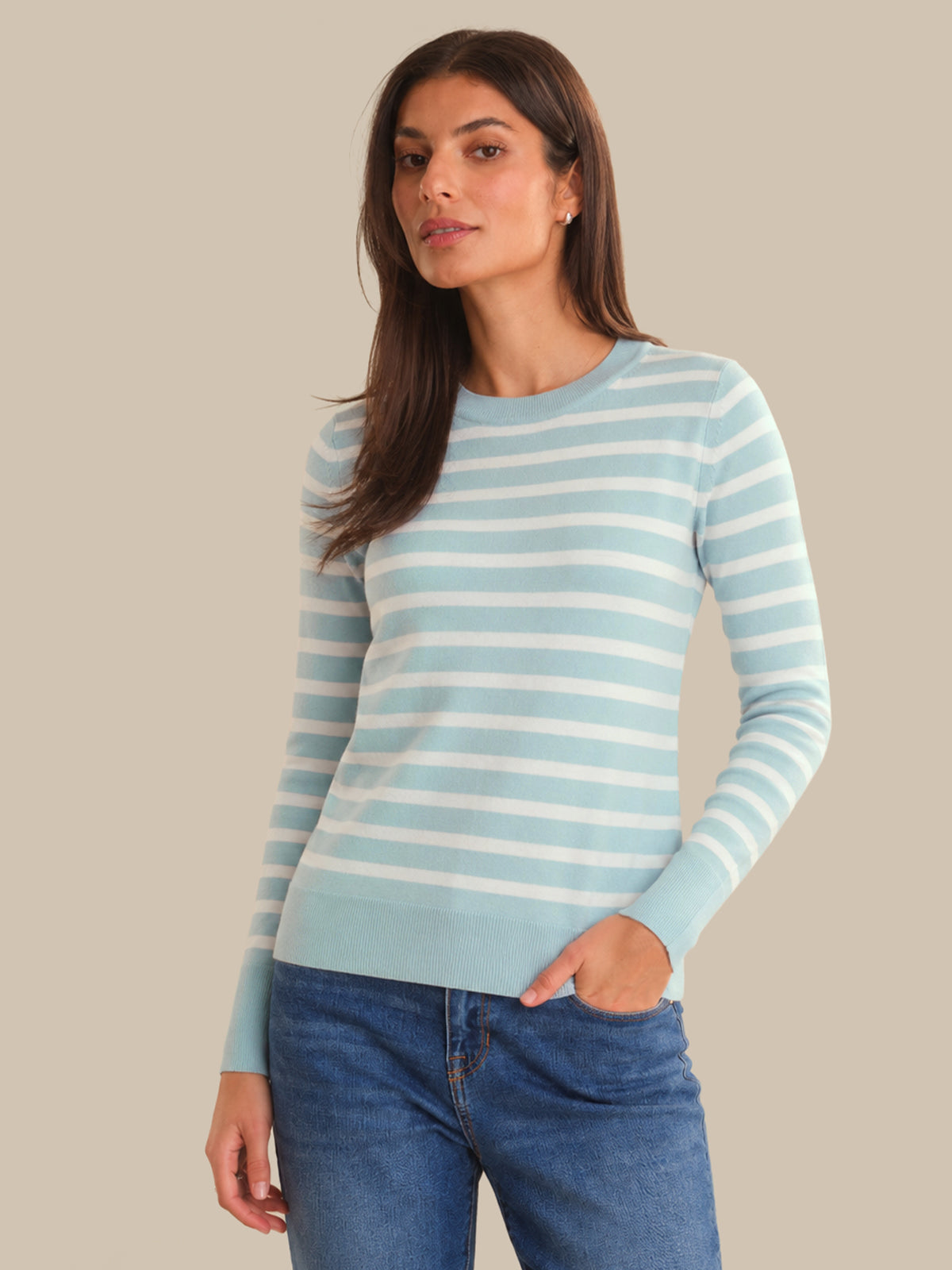 Woman wearing a light blue and white striped sweater with blue jeans on a beige background