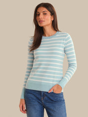 Woman wearing a light blue and white striped sweater with blue jeans on a beige background