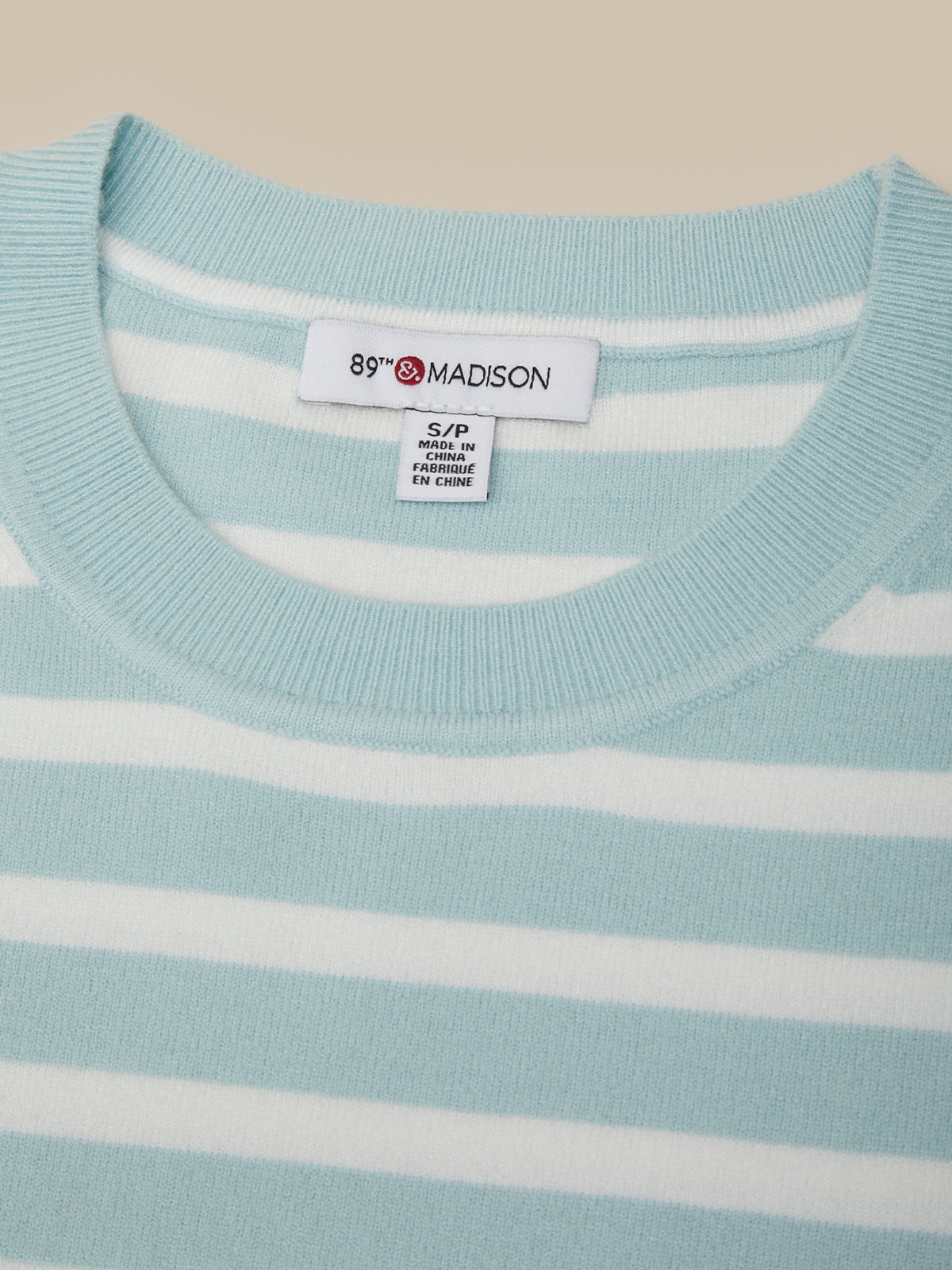 Light blue sweater with white stripes and a visible brand label on a beige background