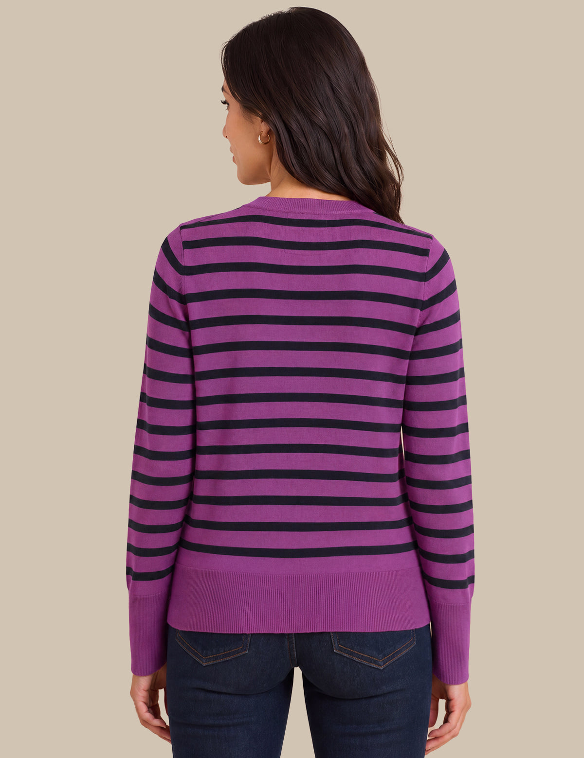 A woman shown from the back wearing a purple and black horizontally striped long-sleeve sweater, paired with dark blue jeans, against a solid beige background.