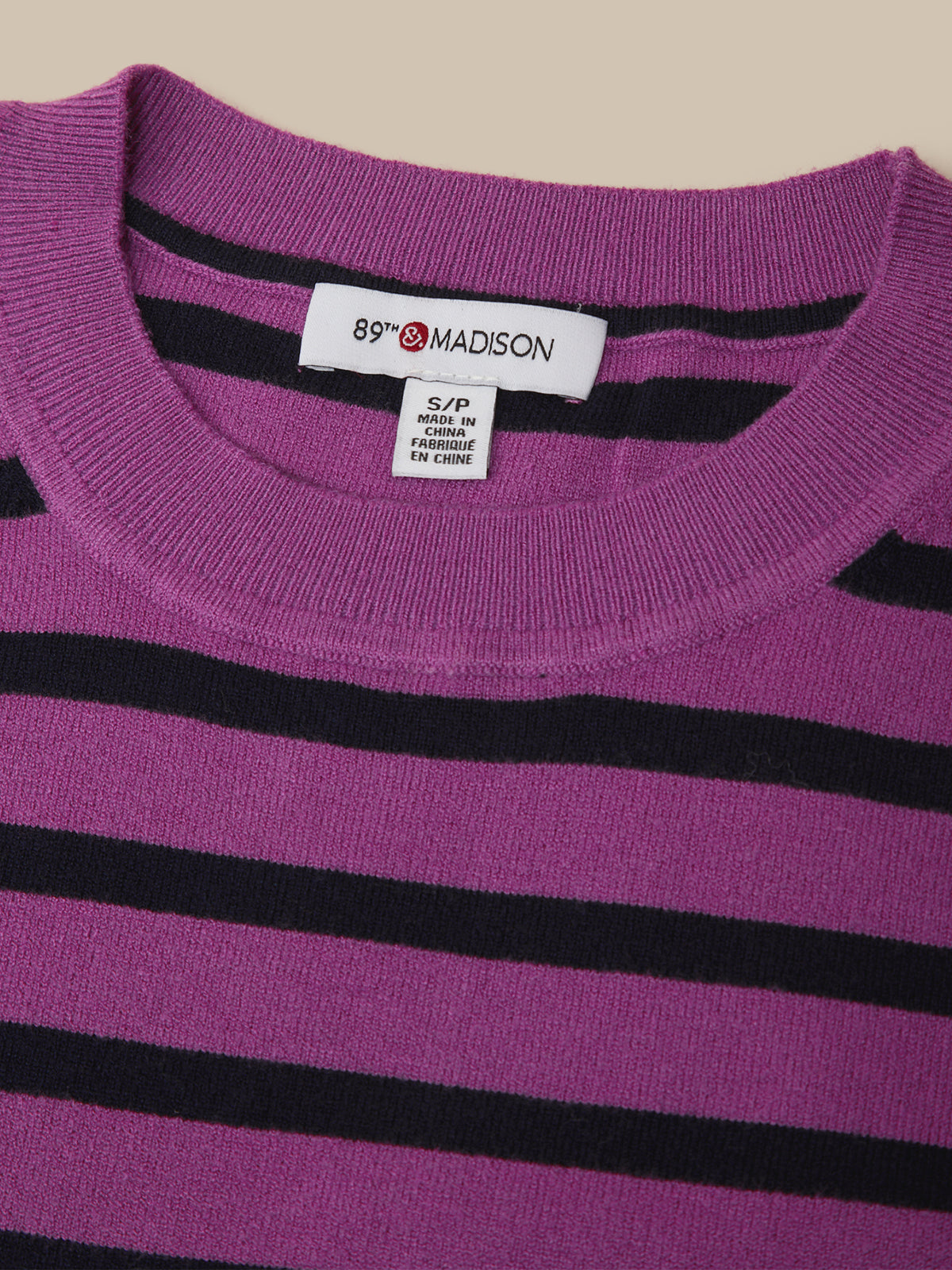 Close-up of a purple knit sweater with horizontal black stripes, showing a white neck label that reads 89th & MADISON.