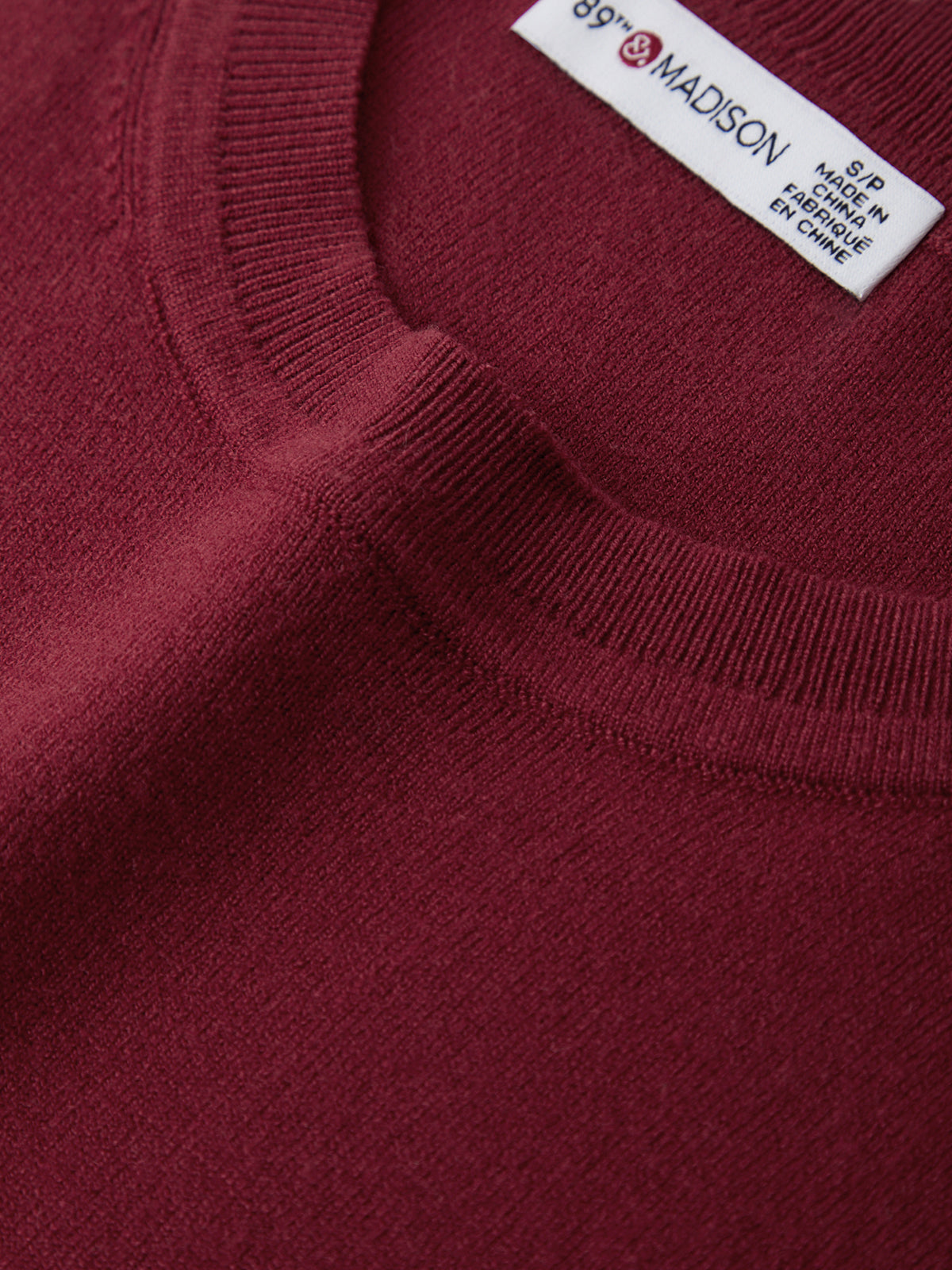 Close-up of a burgundy sweater with a brand label on the collar.