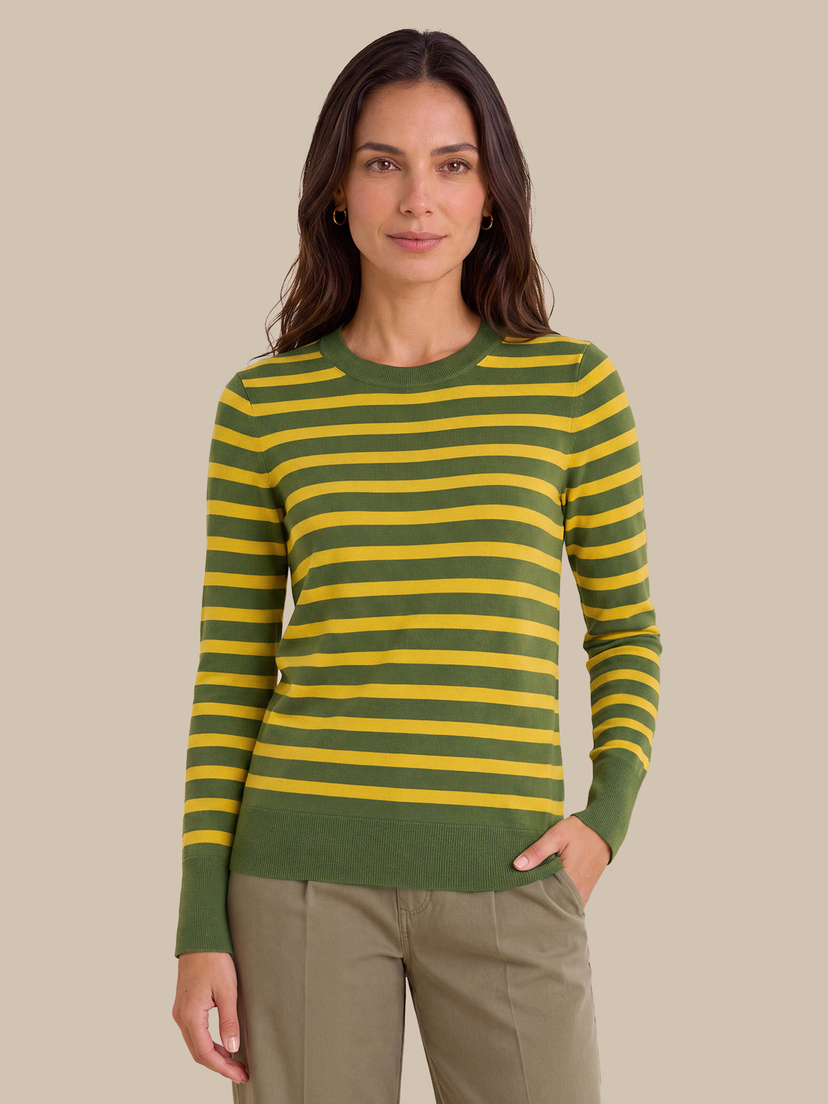 A woman modeling a green and yellow striped long-sleeve knit sweater with olive green ribbed cuffs, collar, and hem, paired with khaki pants, against a solid beige background.