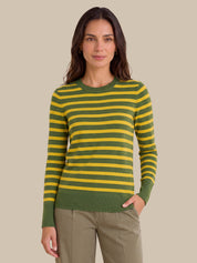A woman modeling a green and yellow striped long-sleeve knit sweater with olive green ribbed cuffs, collar, and hem, paired with khaki pants, against a solid beige background.