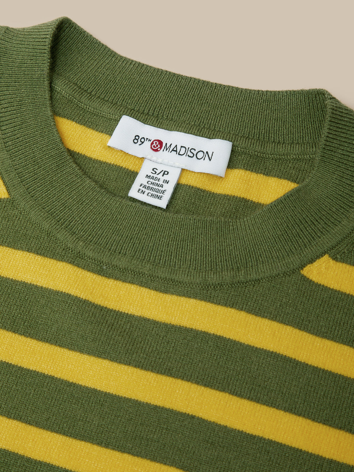 Close-up of a ribbed knit crewneck sweater with horizontal olive green and mustard yellow stripes, showing a white neck label that reads 89th & Madison.