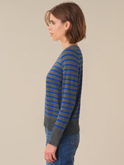 Woman wearing a gray and blue striped sweater against a beige background