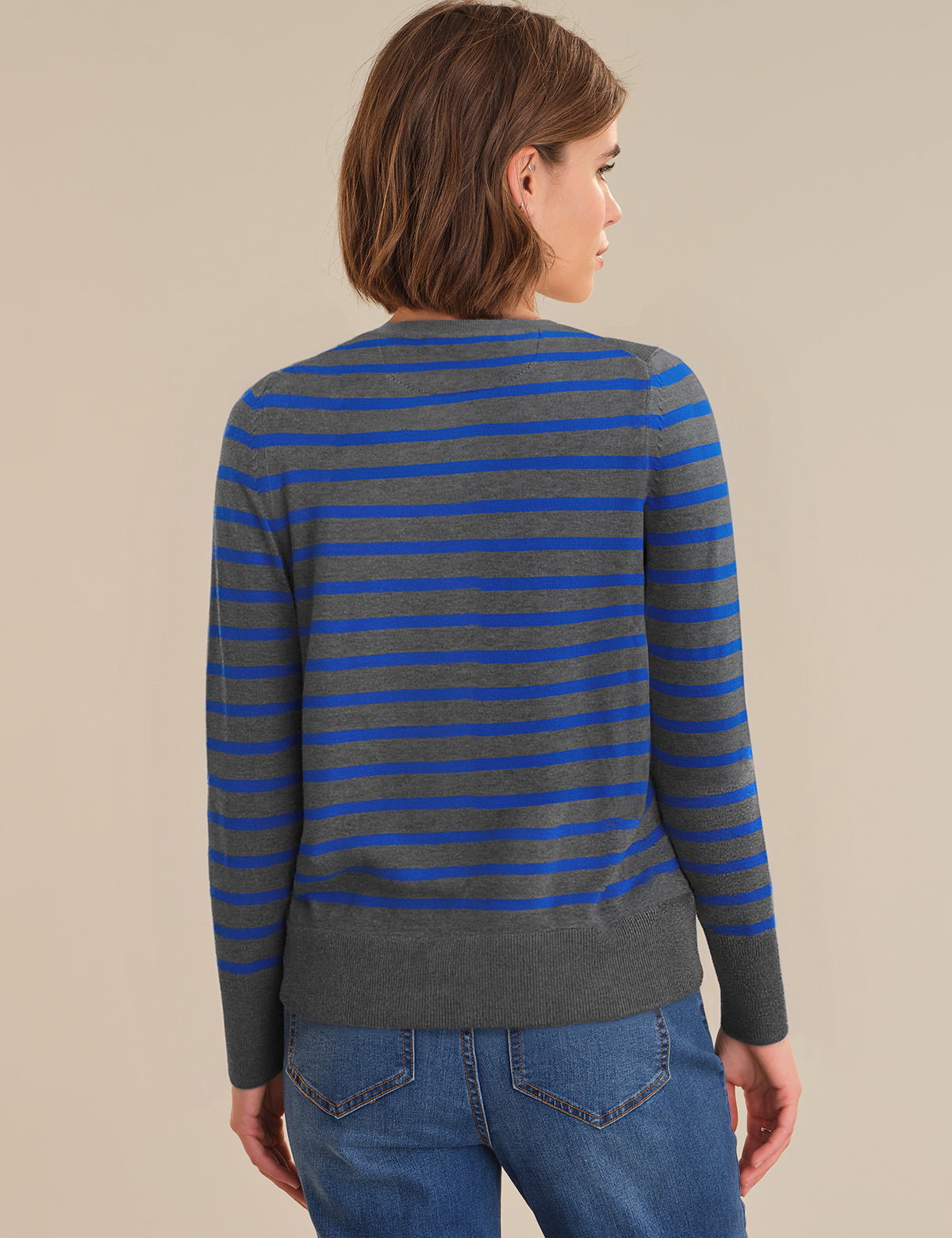 Person wearing a gray and blue striped sweater with blue jeans on a beige background