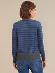 Person wearing a gray and blue striped sweater with blue jeans on a beige background