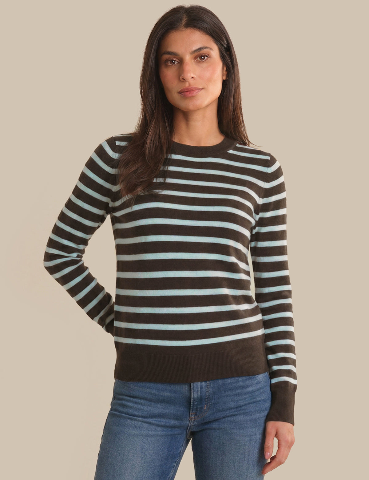 Woman wearing a striped sweater and jeans against a beige background