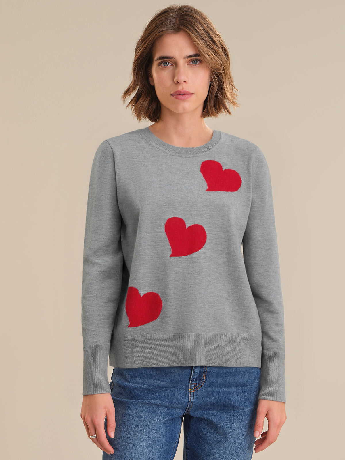 Woman wearing a gray sweater with red heart patterns on a beige background