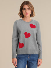 Woman wearing a gray sweater with red heart patterns on a beige background