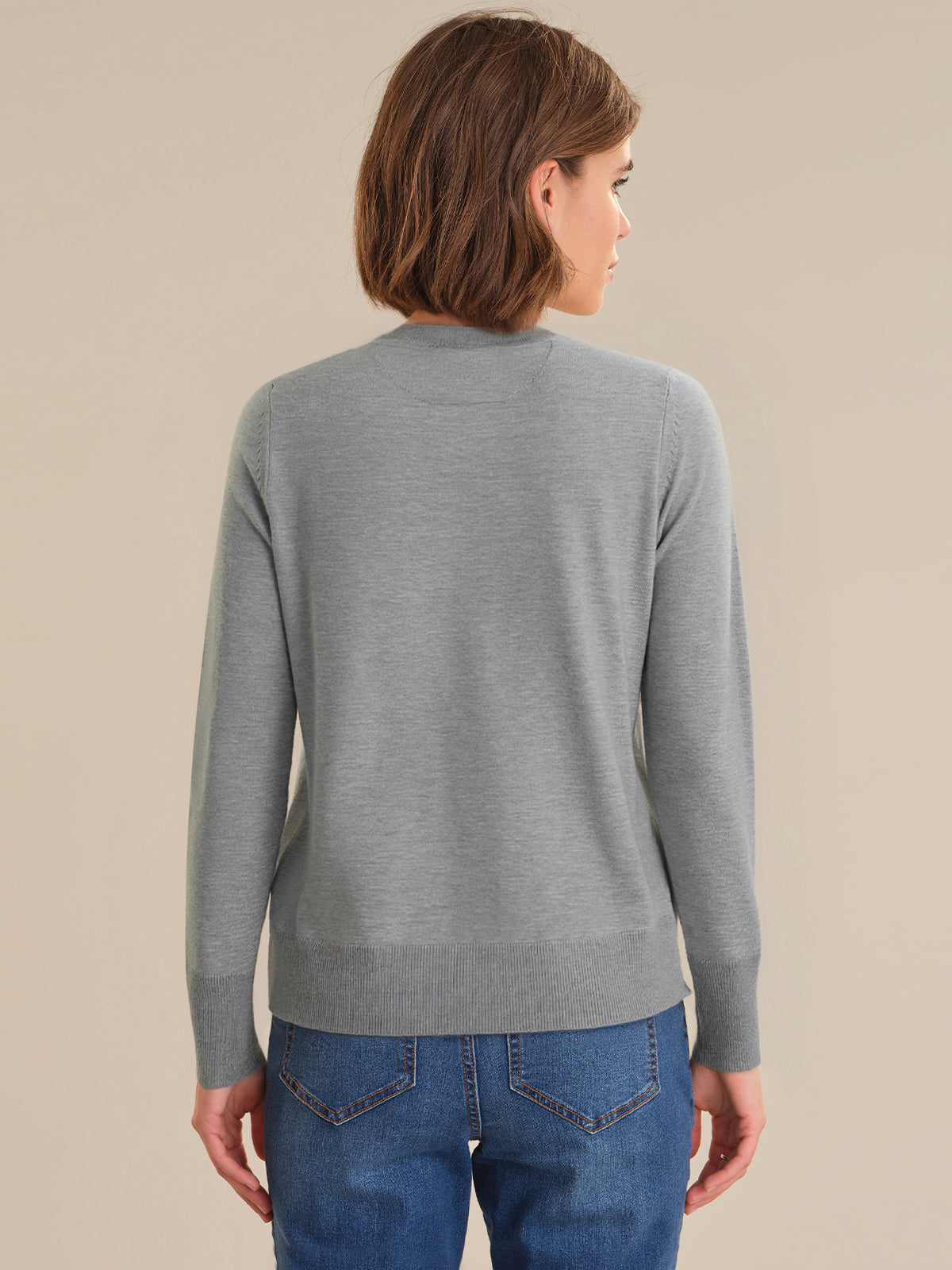 Person wearing a gray sweater and blue jeans on a beige background