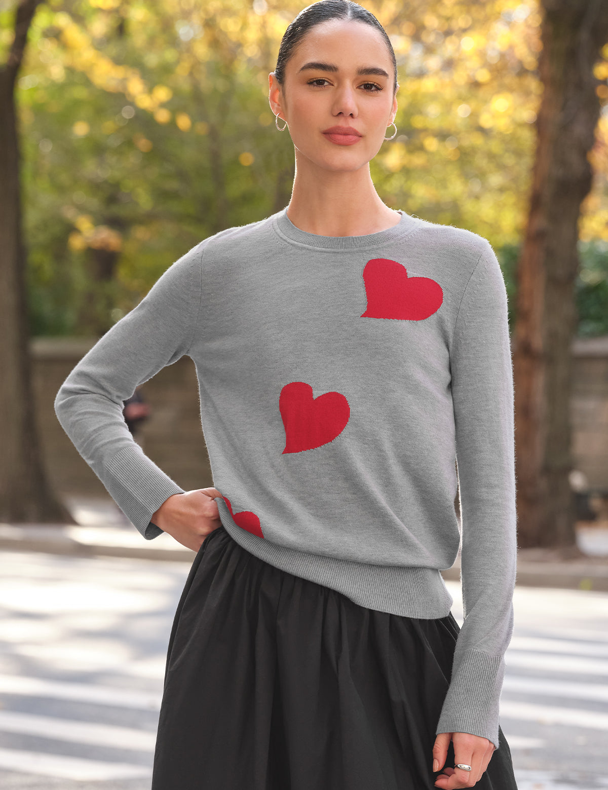 Woman wearing a gray sweater with red heart patterns outdoors.