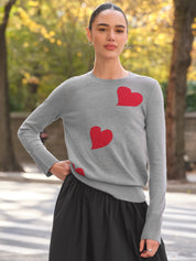 Woman wearing a gray sweater with red heart patterns outdoors.