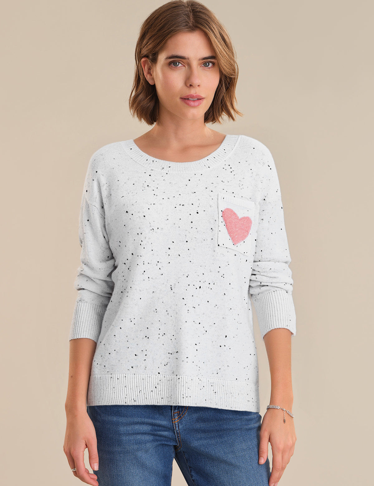 Woman wearing a light gray sweater with a pink heart design on a beige background