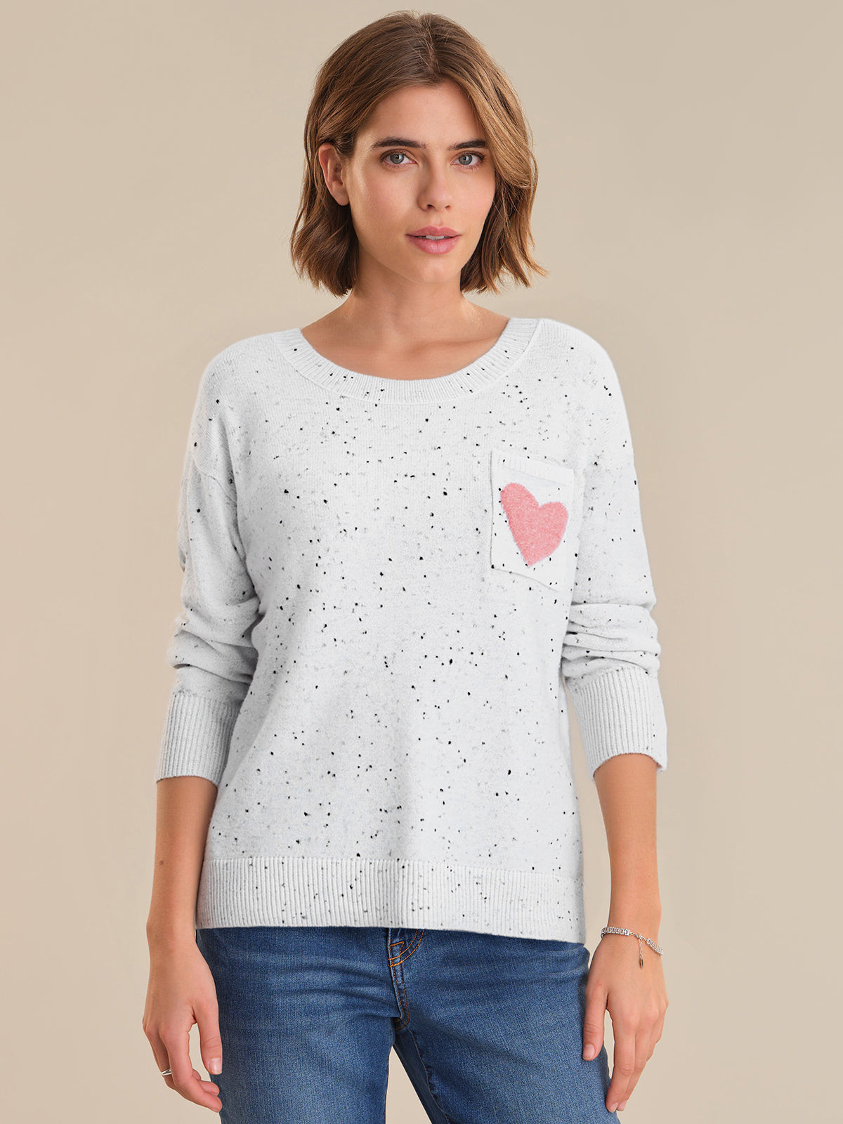 Woman wearing a light gray sweater with a pink heart design on a beige background
